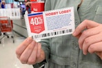 A woman holding a Hobby Lobby coupon near the checkout in a craft store.