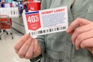 A woman holding a Hobby Lobby coupon near the checkout in a craft store.