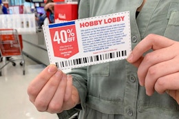 A woman holding a Hobby Lobby coupon near the checkout in a craft store.