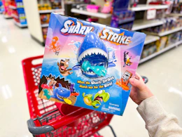 hand holding a shark strike game over a target cart