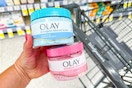 person holding 2 olay body scrubs over a walgreens cart