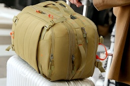 Tolaccea Carry on Travel Backpack Khaki resting on a rolling carry on aluminum suitcase.
