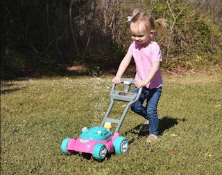 a little girl playing with a toy lawn mower outside