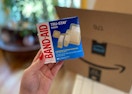hand holding band aid true stay sheer bandages in front of an amazon box