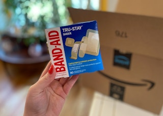 hand holding band aid true stay sheer bandages in front of an amazon box