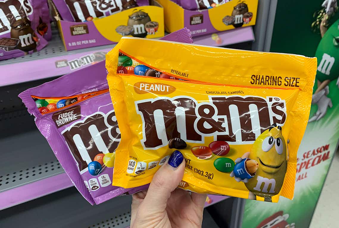 person holding peanut and fudge brownie m&ms candy bags in store