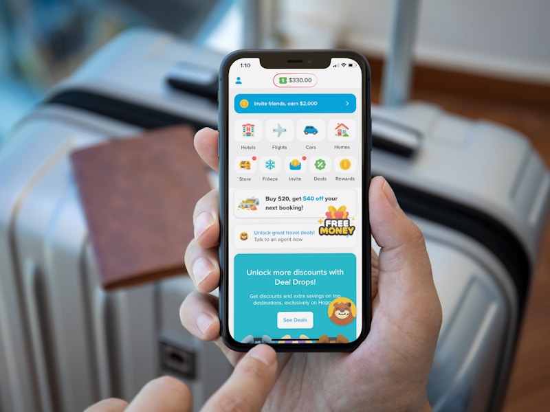 A person using their phone looking at the Hopper travel booking app in front of some packed luggage