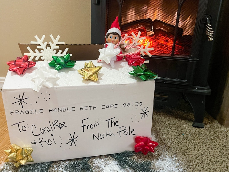 elf on the shelf doll peaking out of a box from the north pole in front of a fake fireplace 