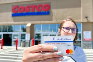 Someone standing outside of a Costco, holding up their HSA card