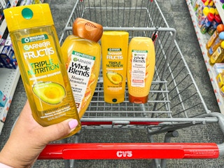 hand holding a bottle of Garnier Fructis and Whole Blends shampoo in front of cart