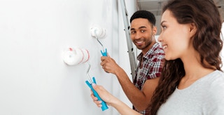 couple rolling white paint on wall together