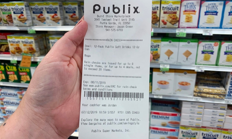 Hand holding a Publix rain check printout in front of cracker selection in store. 