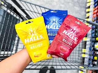 hand holding three bags of Halls cough drops