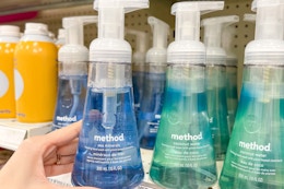 A Method hand soap held out by hand next to other hand soaps sitting on a store shelf.