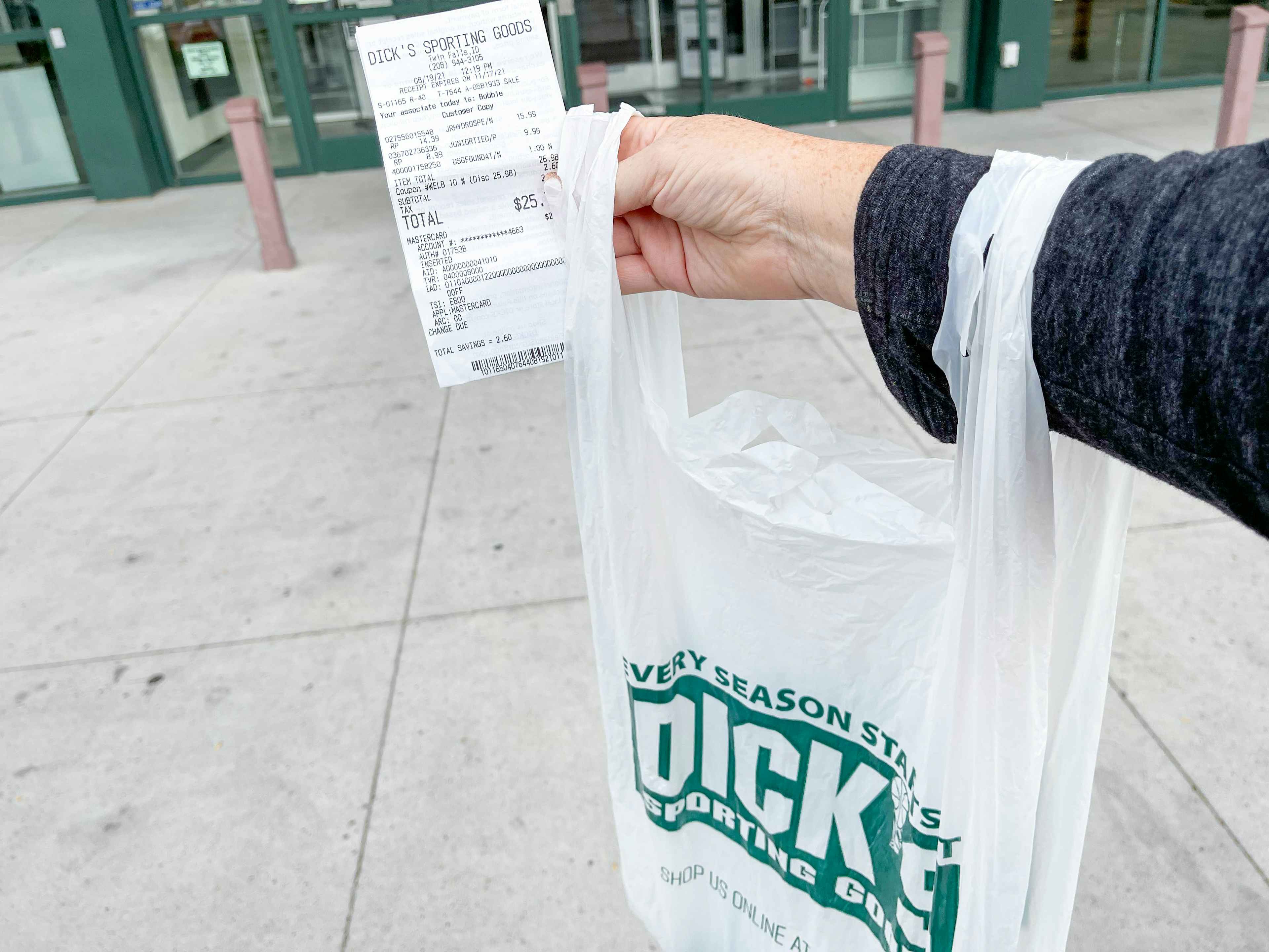 holding a bag and receipt in front of dicks sporting goods