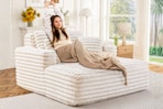 Lifestyle image of the beige Muumblus Oversized Chaise Lounge Chair with woman lounging in home setting