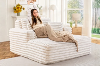 Lifestyle image of the beige Muumblus Oversized Chaise Lounge Chair with woman lounging in home setting