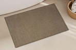 brown bath mat on floor in front of tub