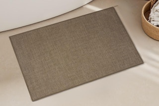 brown bath mat on floor in front of tub