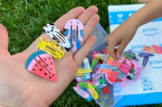 a hand holding colorful hair clips over grass and an Amazon mailer