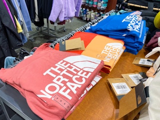 A variety of The North Face shirts folded on a shelf in Dicks Sporting Goods