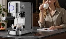 an espresso machine next to a person drinking coffee