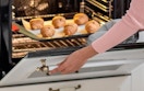 a person pulling out muffins from an oven