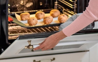 a person pulling out muffins from an oven