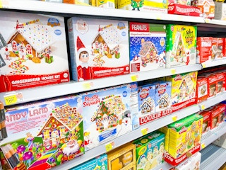 A young boy working on decorating a gingerbread house with bowls of different candies on the table.