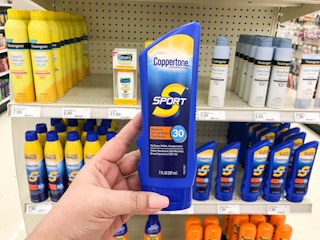 A person's hand holding a bottle of Coppertone Sport sunscreen in front of a shelf of more sunscreen at Target.