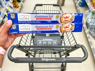 hand holding two boxes of Complete Home aluminum foil in front of shopping cart