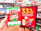 A hand holding a box of candy canes next to a 33% off sign for Kroger's candy sale.