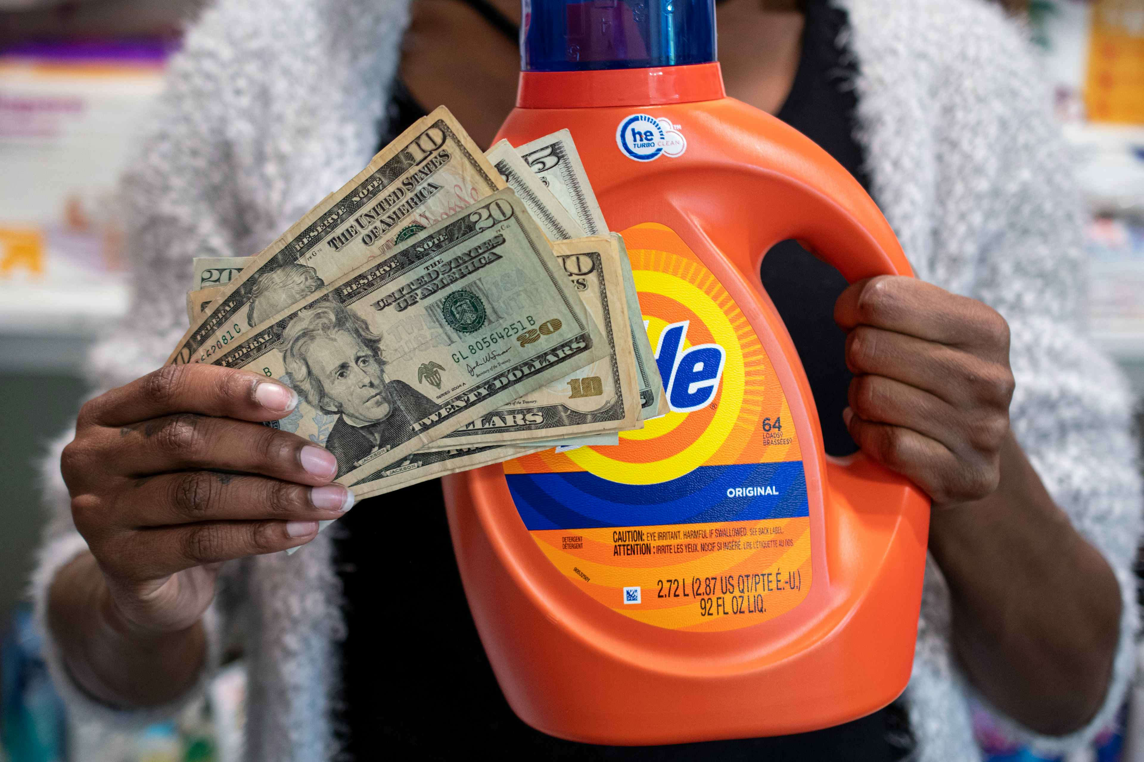 A person holding a stack of cash next to a bottle of Tide laundry detergent.