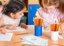 pencils in cups on a table with kids drawing 