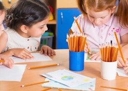 pencils in cups on a table with kids drawing 