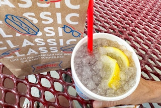 a person holding a sonic drink in front of sonic to go bag