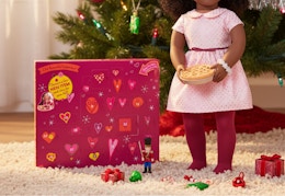 magenta colored advent calendar in front of a Christmas tree and next to an 18-inch doll with accessories