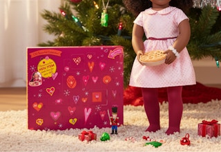 magenta colored advent calendar in front of a Christmas tree and next to an 18-inch doll with accessories