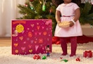 magenta colored advent calendar in front of a Christmas tree and next to an 18-inch doll with accessories