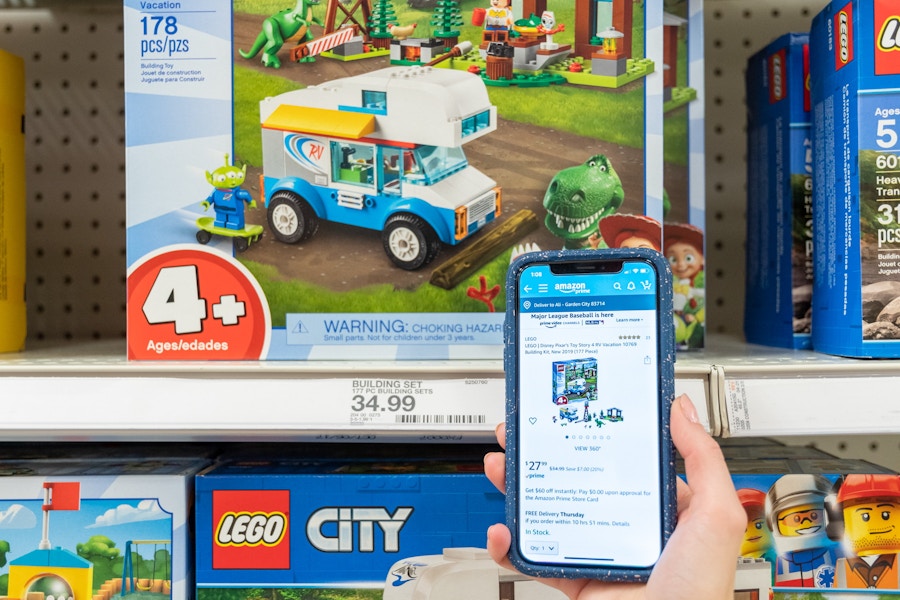 A hand holding a phone showing an Amazon listing for a toy in front of the same toy on the shelf at Target