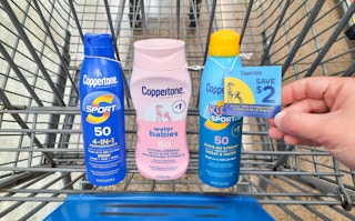 Coppertone Sunscreen products in Walmart shopping cart. Hand is holding a $2 coupon that is attached to one of the products.