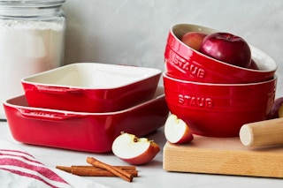 A set of red Staub bakeware on a striped linen cloth