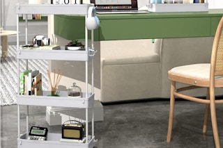 a rolling cart with books and decor next to a green table and wooden chair in a room
