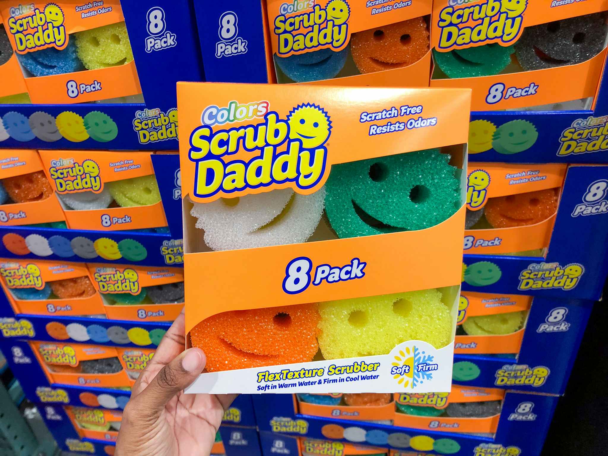 person holding an 8-pack of scrub daddy sponges in front of a display