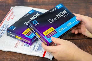 someone picking up some Covid-19 test kits on top of a USPS package