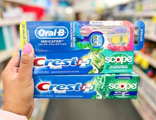hand holding two Crest with Scope Toothpaste and one Oral-B toothbrush