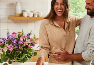 A couple standing next to a bouquet of flowers on a kitchen counter. 