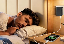 a person laying on a bed next to a phone charging on a nightstand