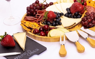 a bamboo cheese board and knives with cheese and fruit