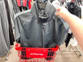 someone holding a mens jacket by a jcpenney cart